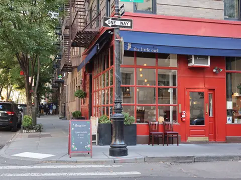 A red corner cafe with sidewalk tables on a leafy New York street